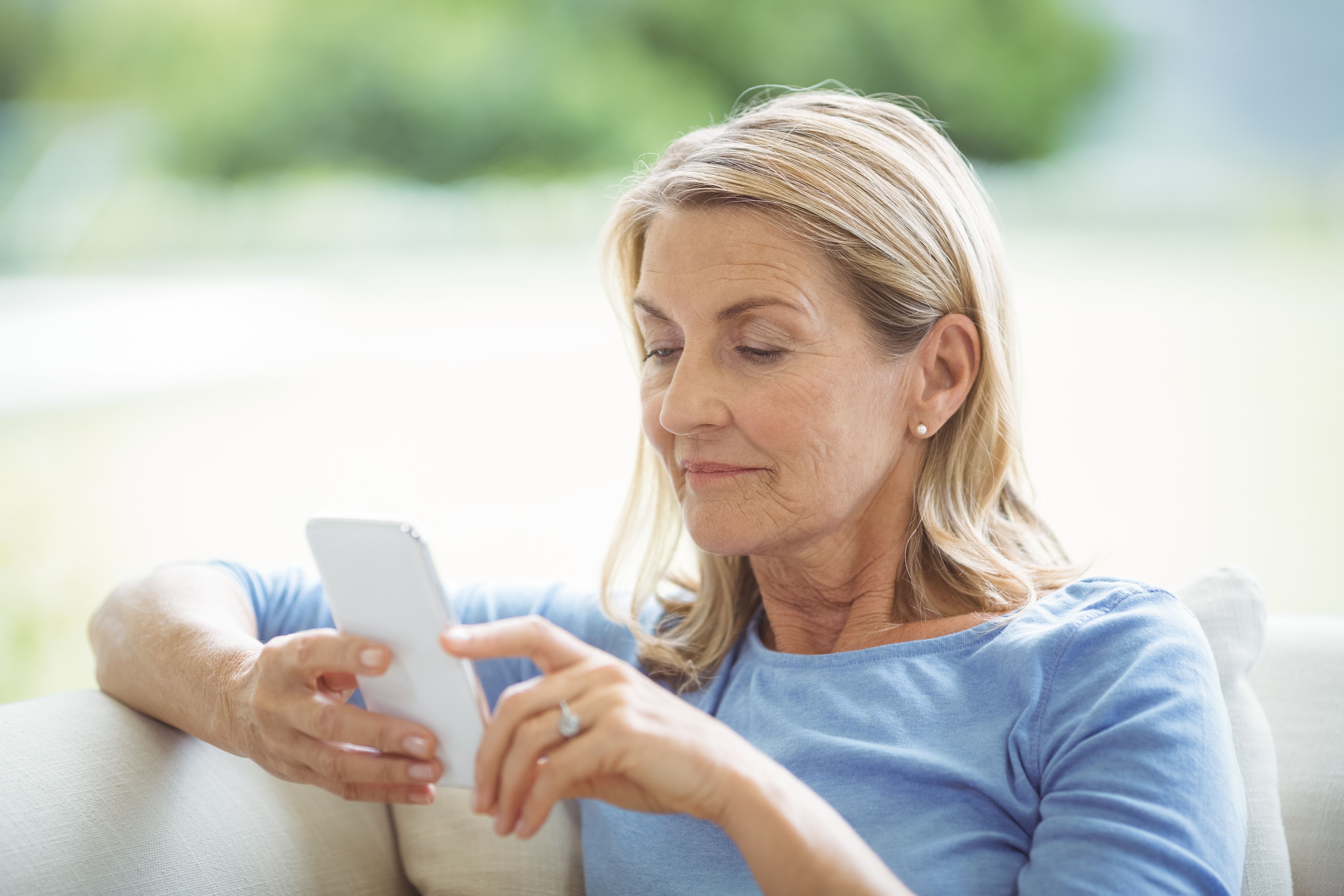 A woman comfortably using a smartphone on a sofa